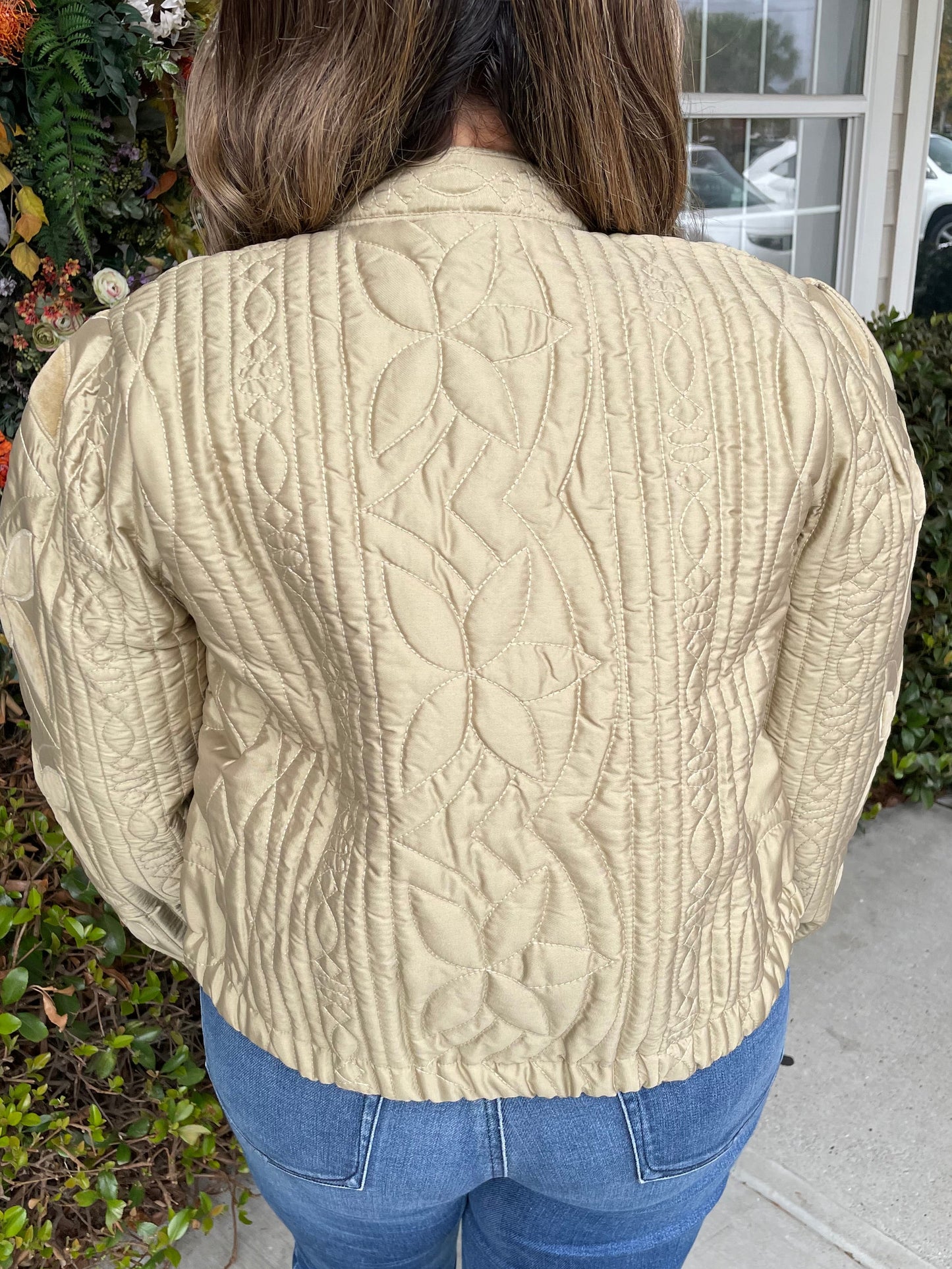 Person wearing a beige quilted jacket and blue jeans outdoors.